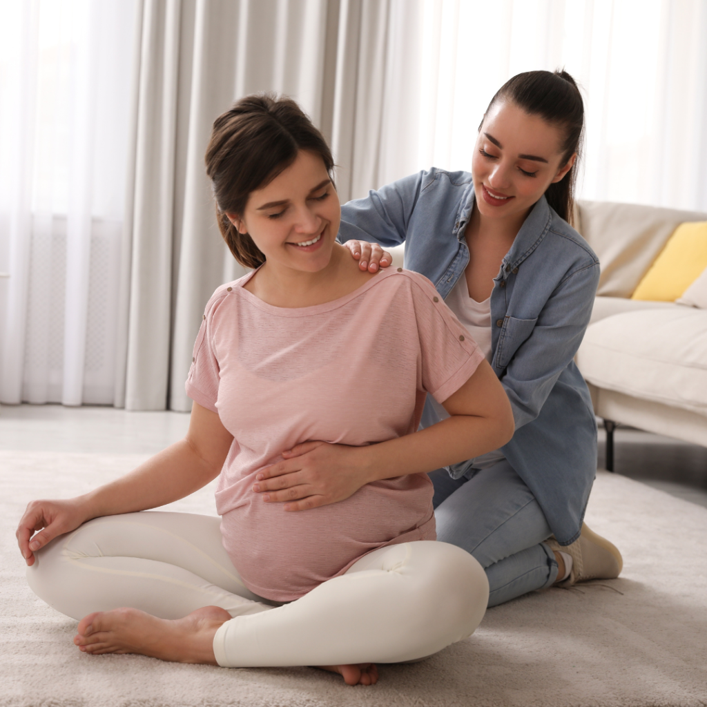 A pregnant woman with another woman helping rub her back.