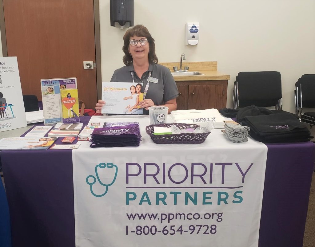 Woman sits at table with handouts about Priority Partners.