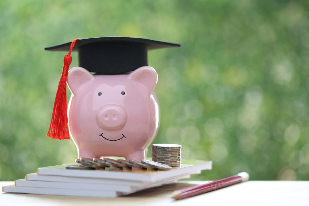 piggy bank sitting on top of books with a graduation cap