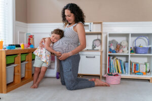 pregnant mom sitting and hugging in a playroom with toddler